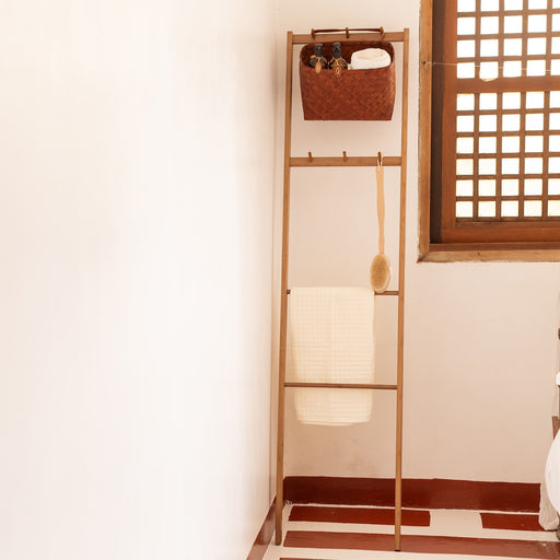 Wooden ladder shelf against a wall with a basket and lamp on it.